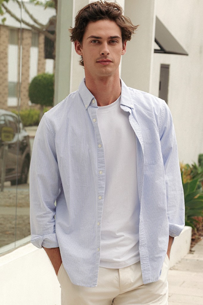 Ivan in a striped oxford shirt over a white tee, standing on a sunlit street