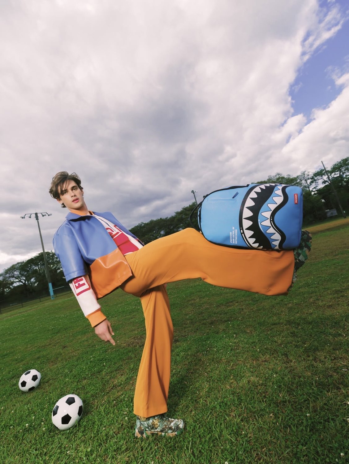 Ivan mid-kick on a soccer field wearing a Sprayground shark backpack